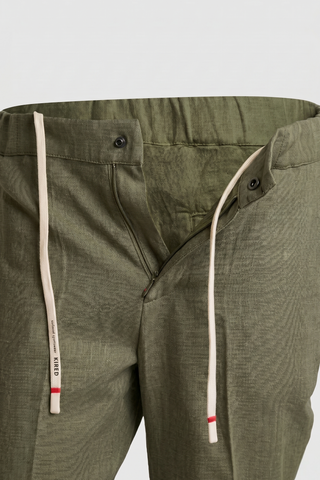 Close-up of olive green pants with a white drawstring on a light gray background